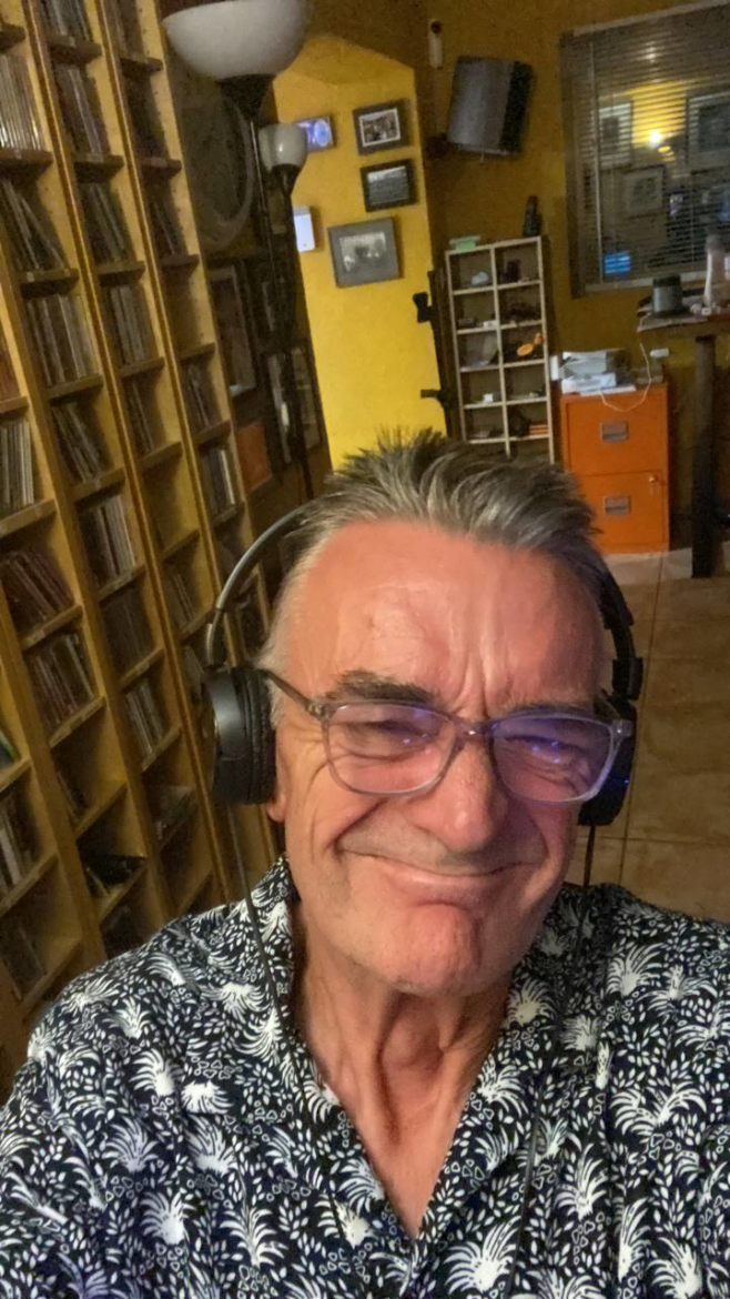 Photo of Robbie Cassels sitting in front a large wall unit full of CDs.